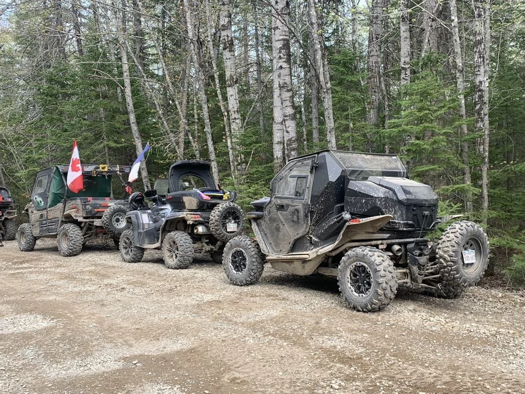 A group of ATVs and side-by-sides parked on a forest trail