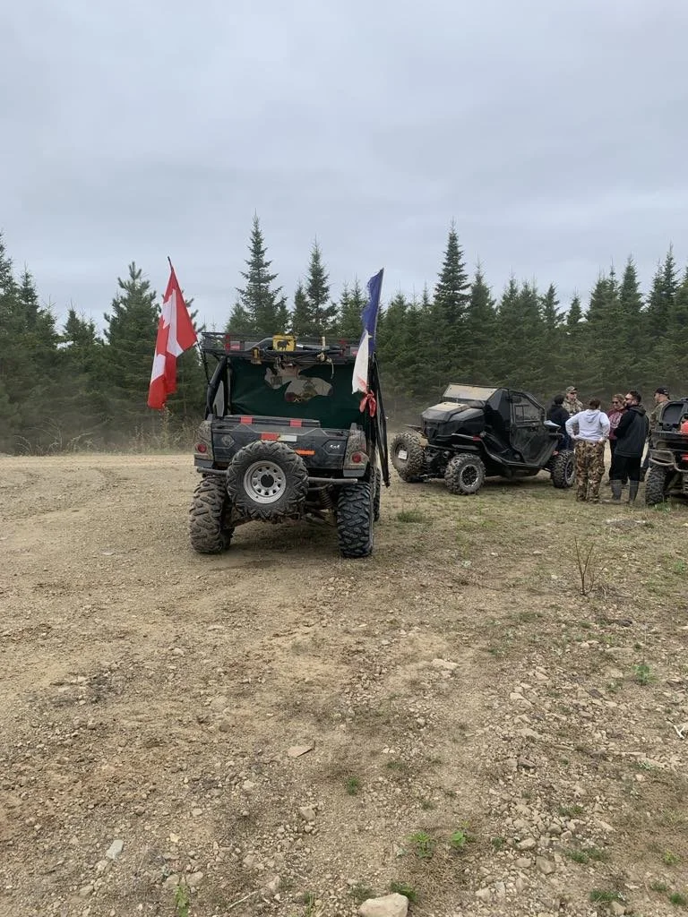 A UTV with flags parked on a trail in the spruce woods